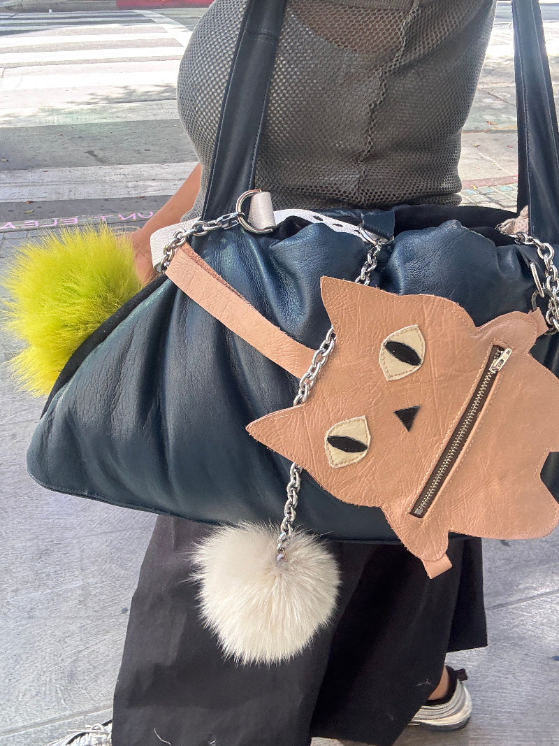 Cat-shaped bag with fur pom-poms on a person's shoulder