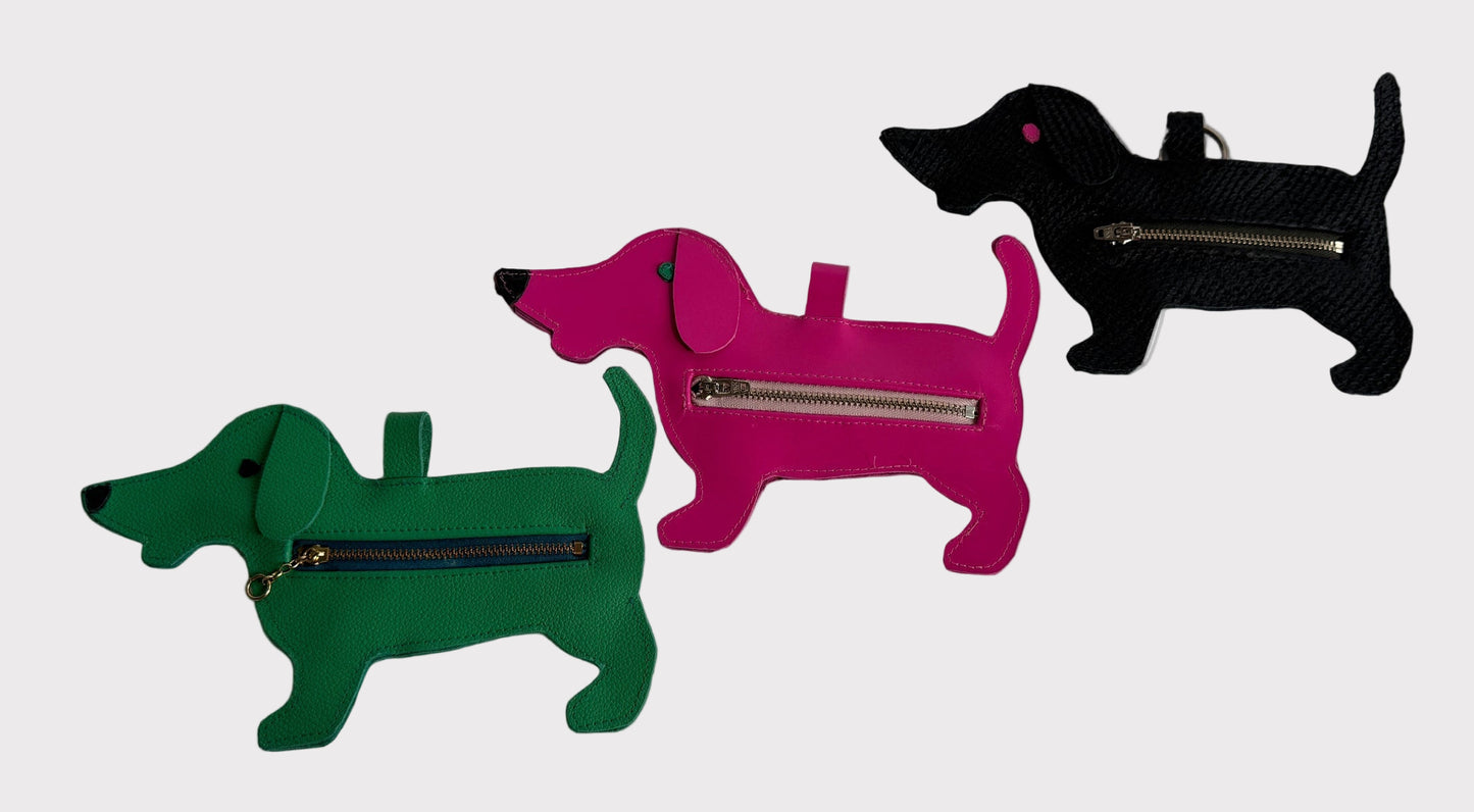 Three dog-shaped dog waste bag dispensers in green, pink, and black on a white background