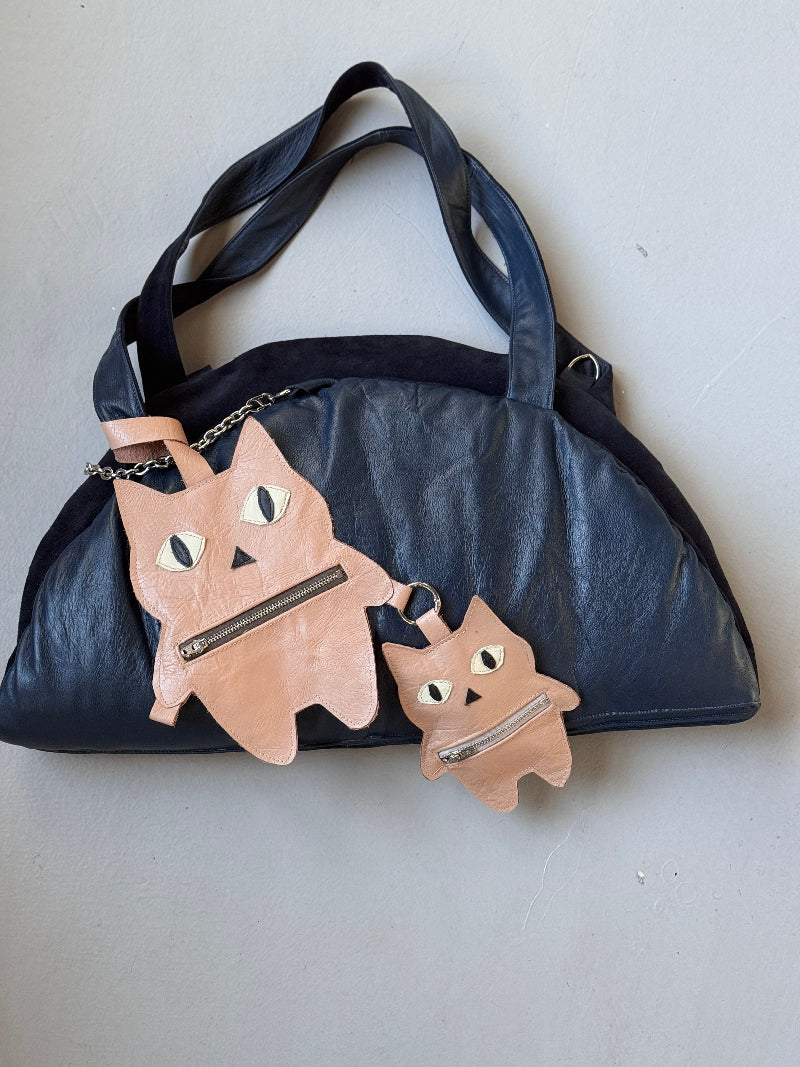 Black handbag with pink cat-shaped zipper pulls on a light gray background