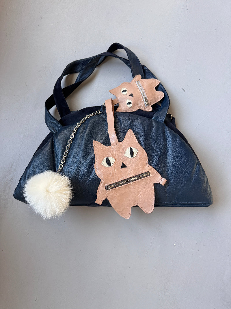 Navy blue handbag with pastel big and small fat cat charms on a light gray background