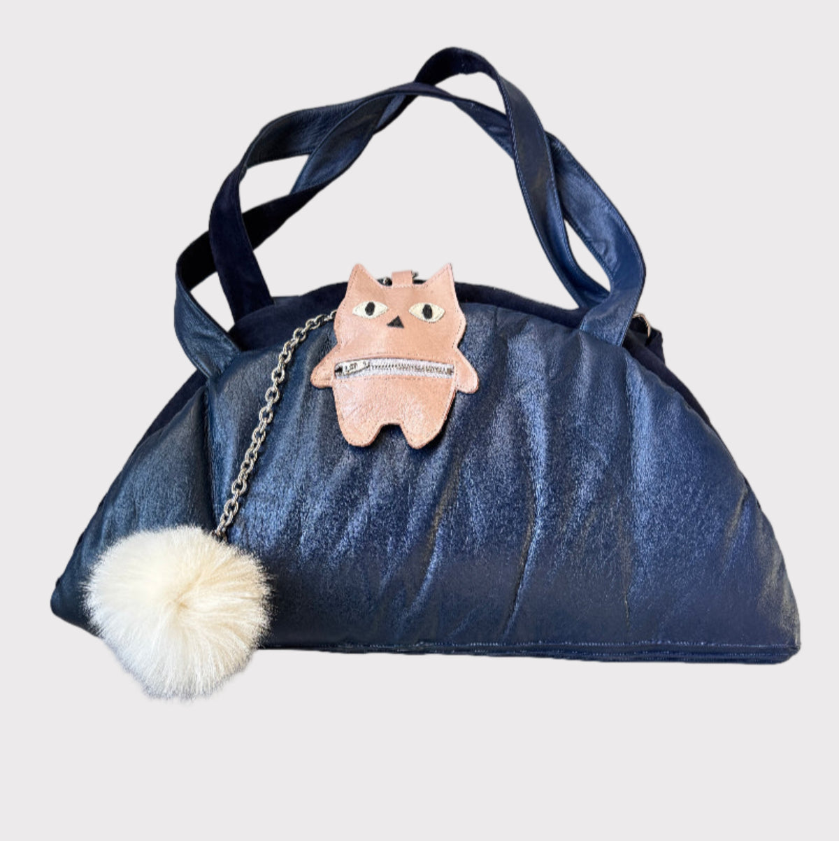 Blue handbag with a fluffy pom-pom and small plush toy on a light gray background