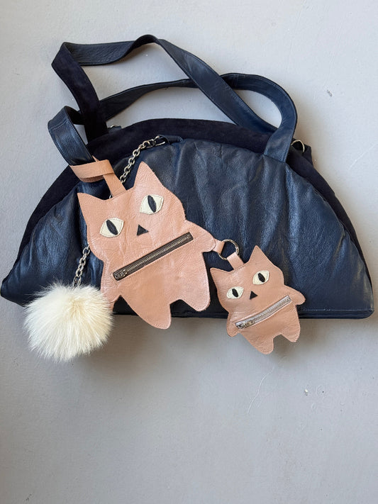Navy blue handbag with cat-shaped pouches and a fluffy pom-pom on a light gray background