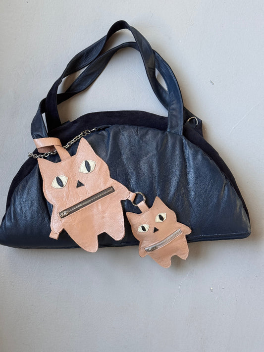 Black handbag with pink cat-shaped zipper pulls on a light gray background